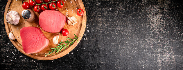 Raw tuna on a cutting board with garlic, tomatoes and spices. 