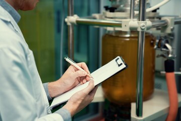 Closeup apothecary scientist using a clipboard and pen to record information from a CBD oil...