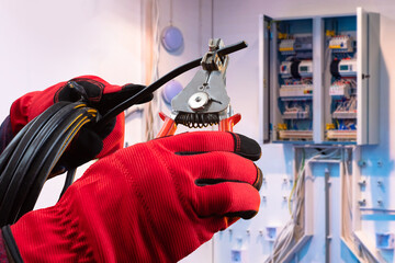 Wire cutting process. Black cable in hands of electrician. Master prepares wire for connection to electrical panel. Cable management. Hands in red gloves cut network wire. Electrical cabinet blurred