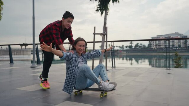 Cheerful son pushing his mother on a skateboard and laughing. Wild and crazy