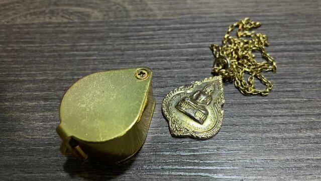 Gold mini folding pocket magnifier lens on table with Thai amulet buddhist sacred talisman for fortune and protection meditation on golden necklace. Traditional Thai religious superstition concept