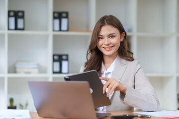 Beautiful Asian businesswoman sitting smiling and happy  with laptop computer in the office. Looking at camera.