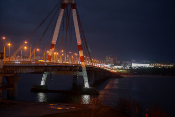 Fototapeta na wymiar A large automobile bridge on which cars drive at night. A bridge with large columns and lighting.