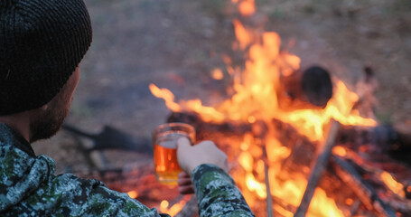 Man with cup of tea the fire in the forest. Human looks at the bonfire and drinks tea on the nature...