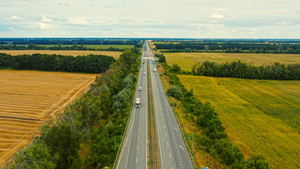 Aerial view of a motorway in summer on a cloudy day. Aerial view of a suburb road with trucks. Drone  above a highway with driving cars.