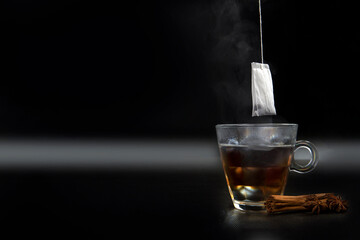 Glass of hot tea with tea bag hanging black background copy space,