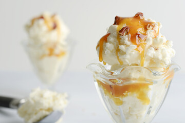 closeup vanilla ice cream with pecans and caramel sauce in glass sundae dish