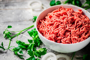 Minced meat in a bowl on a table with parsley and onion rings. 