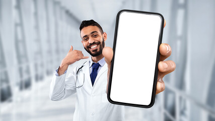 Middle eastern male doctor showing blank smartphone and making call me gesture