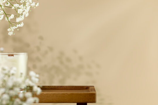 Wooden empty podium for beauty or spa products, cosmetics on natural beige background with flowers and candle. Scene stage showcase for product, promotion sale or advertising. Front view, copy space