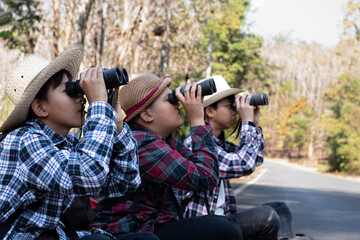 Obraz premium Asian boys are using binoculars to do the birds' watching in tropical forest during summer camp, idea for learning creatures and wildlife animals and insects outside the classroom.