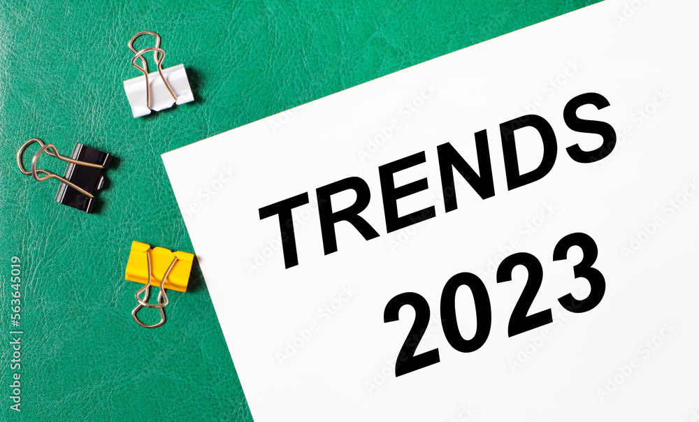 Poster multi-colored paper clips and a sheet of paper with the text trends 2023 on a green notepad.