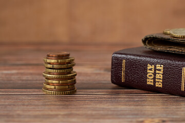 Stack of coin money, holy bible book and old wallet on wooden table. Copy space, a closeup. Christian biblical concept of tithing, giving, and religious offering.