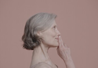 CU Portrait of beautiful 60s grey-haired mature senior adult female posing without makeup against light brown background. Studio shot, soft lighting. No make up, clean skin