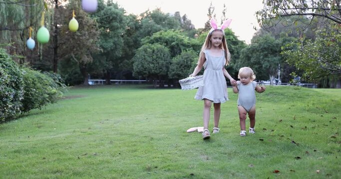 Two Children Wearing Bunny Ears when Pick Up painted Easter Egg Hunt In Garden or park. Cute caucasian baby and sister spending time together on backyard. Slow motion