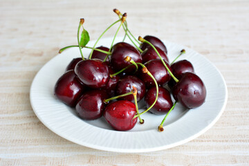 heap of shiny garden cherries on white saucer with water drops isolated, macro
