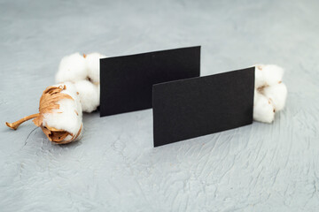 Two black business cards next to cotton flowers on gray cement textured backdrop,