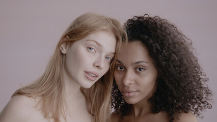 Candid portrait of two beautiful 20s females, African-American Black and Caucasian, posing against solid background, no make-up, studio shot, soft lighting