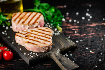 Grilled tuna on a cutting board with parsley and tomatoes. 