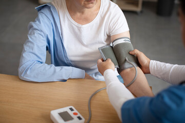 Doctor measures blood pressure with tonometer of senior european female patient in clinic office...