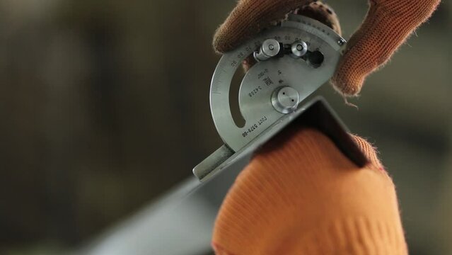 professional engineer in orange gloves measures angle section of metal detail with special protractor standing at plant workplace closeup