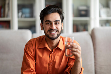 Happy arab guy holding glass of water, home interior