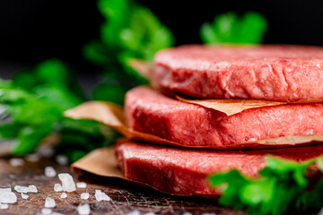 Raw burger on a table with greens and salt. 