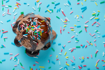 top view of chocolate scoop of sundae ice cream covered with chocolate icing and strewed sprinkles on blue, festive background for Valentines day, birthday, holiday and party time