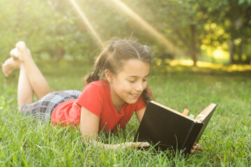 Little girl with a book in the garden. Kid is readding a book on hands. outdoors in summer day. Countryside