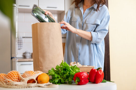 Woman At Home Getting Groceries Out Of A Shopping Bag With Grocery Ordered From Internet. Fresh Organic Vegetables, Greens And Fruits. Kitchen Interior.  Food Delivery Concept