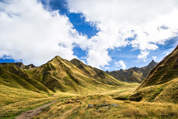 une silhouette d'homme marchant dans une montagne verte sous un ciel bleu et des nuages blancs