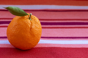 Close-up of ripe orange with green leaf on striped background