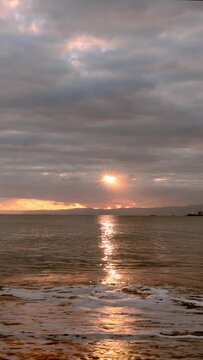 七里ガ浜に打ち寄せる波と江の島と輝く夕陽（縦型ビデオ4K）