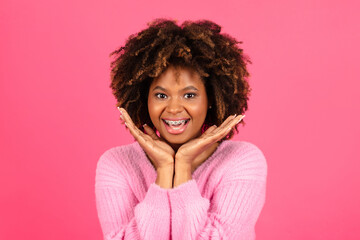Laughing millennial african american curly lady with braces in casual look at camera isolated on pink background