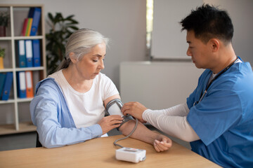 Serious mature korean doctor measures pressure with tonometer of old european woman patient in clinic
