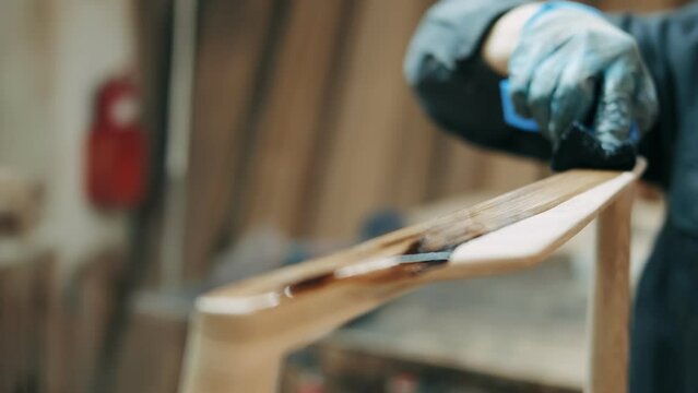 Professional carpenter working in workshop with wooden products, joiner applying brown colour paint on wood furniture, worker varnishing wood for further furniture. High quality 4k footage