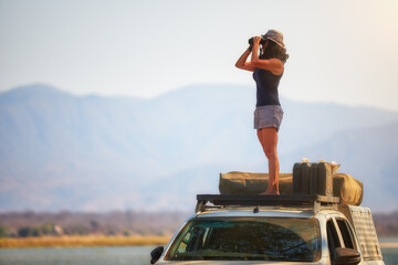 On safari in Zambia: Silhouette of a Fit Woman standing on the roof of safari car, observing...