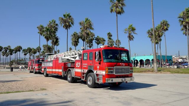Red fire rescue vehicles parked on road at Venice beach with palm trees and clear blue sky in the background during sunny day