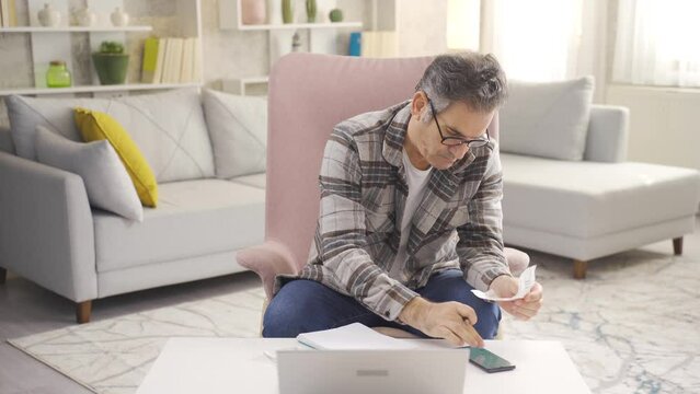 Focused middle-aged man holding shopping and debt bills.
Serious mature man managing family budget at home.
