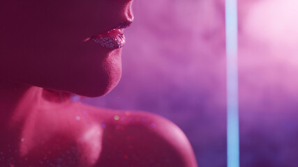 Fototapeta premium Neon beauty. Glitter skin. Nightclub look. Closeup of woman face with metallic lips sparkling bare shoulder on blur pink color light smoke free space background.