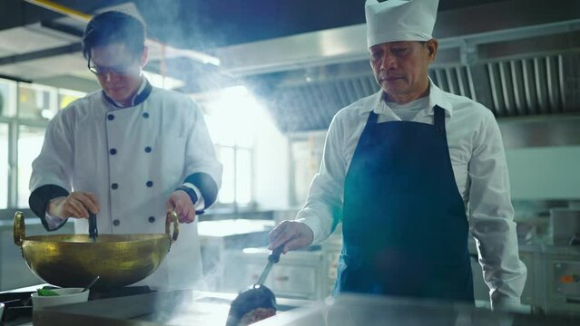 Professional chef cooking at ketchen together. Team of professional cooks in uniform preparing meals for a restaurant in kitchen. Chef, Lifestyle, Education, Happiness, Cheerful concept.