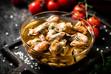 Pickled mussels in a bowl on a cutting board with cherry tomatoes. 