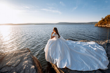 Fototapeta na wymiar Romantic beautiful bride in white dress posing with sea and mountains in background