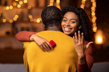 Cheerful black woman showing engagement ring, hugging her fiance