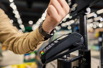 Close up of a man paying with smart watch at supermarket at self-service checkout.