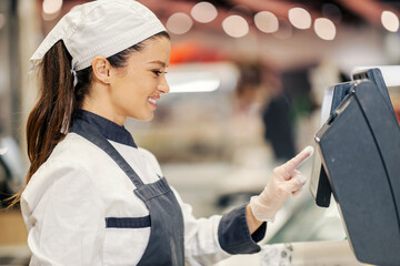 Profile of a bakery department worker measuring pastry on scales while standing in supermarket.