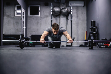 Obraz na płótnie Canvas Exercise chest and arms on a training bar. A man in sportswear leaning his knees on the floor and holds his hands on a barbell. Strength, powerful body and physical practice