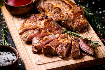 Slices of grilled steak pork on a wooden cutting board. 