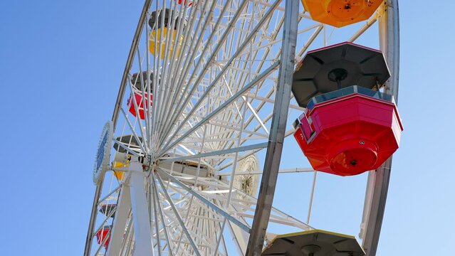 Ferris wheel and roller coaster rides and people exploring shops at the Pacific amusement park on the Santa Monica Pier.