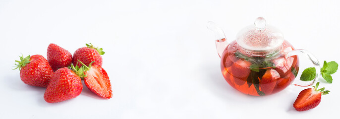 Strawberry tea in the glass teapot and ripe strawberry on the white background. Copy space. Close-up.